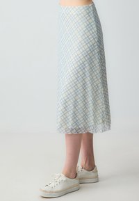 Lichtblauwe geruite midi-skirt van doorzichtig materiaal, met een vloeiende snit en een comfortabele pasvorm. Gecombineerd met witte sneakers.