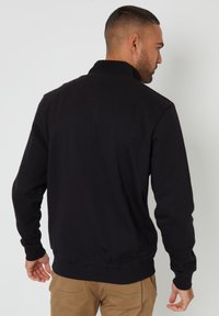 Zwarte sweatshirt met een hoge kraag, geribbelde manchetten en zoom. Glad textuur en minimalistisch ontwerp, bekeken van de achterkant.