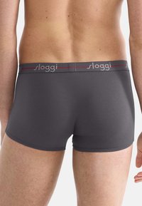 Boxer aderenti grigi con una texture liscia, dotati di una vita con logo grigia e dettagli rossi. Il design offre una forma aderente.