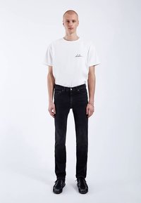 Bílé tričko s krátkým rukávem a černým logem, doplněné černými džínami slim fit a černými teniskami. Minimalistický design, čisté linie.