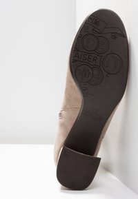 Chaussure en daim beige à bout arrondi, dotée d'un petit talon empilé et d'une semelle en caoutchouc noir texturée, embossée de motifs détaillés.