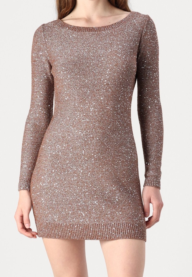 Femme portant une robe marron en maille ajustée, à manches longues, longueur genou, avec des ornements en sequins argentés.