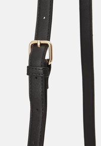 Cintura in pelle nera con una texture liscia, dotata di una fibbia in metallo dorato e fori per la regolazione lungo tutta la lunghezza per la personalizzazione della misura.