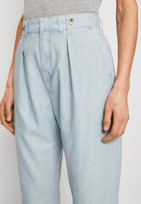 Hellblaue, plissierte Hose aus weichem Stoff, mit einem Knopfverschluss am Bund und seitlichen Taschen, im lässigen Schnitt.