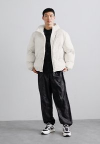 Puffig vit jacka med huva, svart strukturerad topp under, lösa svarta byxor och distinkta vita och svarta sneakers.