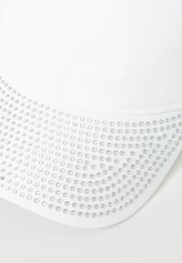White cap featuring a textured brim adorned with multiple clear rhinestones, creating a sparkling pattern contrast against the smooth fabric.