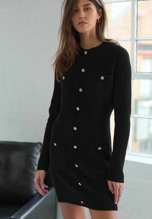 Mustvalge kootud kleit pikkade varrukatega, soonik-tekstuuriga, kahe esipocketiga ning hõbedaste nööpidega keskel ja taskutel.