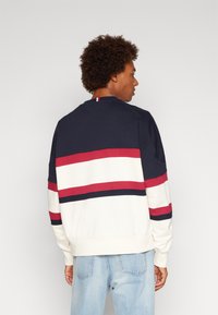 Felpa blu navy con strisce orizzontali rosse e bianche, design a girocollo, tessuto morbido, polsini e orlo a costine. Vestibilità casual.
