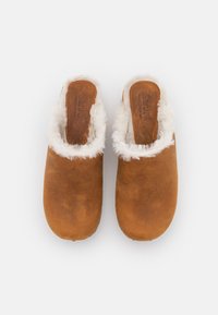 Zoccoli in suede marrone con fodera in ecopelliccia bianca. Design a punta rotonda, stile slip-on e logo impresso sulla soletta. Suola piatta.