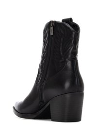 Botín de cuero negro hasta el tobillo con punta afilada, cremallera lateral y diseño de hojas en relieve en el caña. Cuenta con un tacón grueso para mayor soporte.