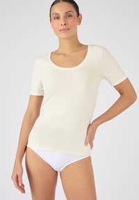 Top crema a maniche corte con colletto scallop, realizzato in materiale morbido; abbinato a biancheria intima bianca. Texture liscia, design semplice.