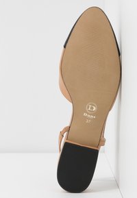 Sål af en tan flad sko med sort hæl og flettet ankelrem, størrelse 37, mærkelogo "Dune London" synligt på sålen.