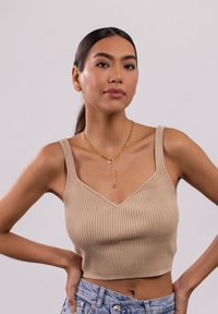 Beiges geripptes Cropped-Top mit V-Ausschnitt und dicken Trägern, kombiniert mit blauen Jeansshorts und einer mehrlagigen goldenen Halskette.
