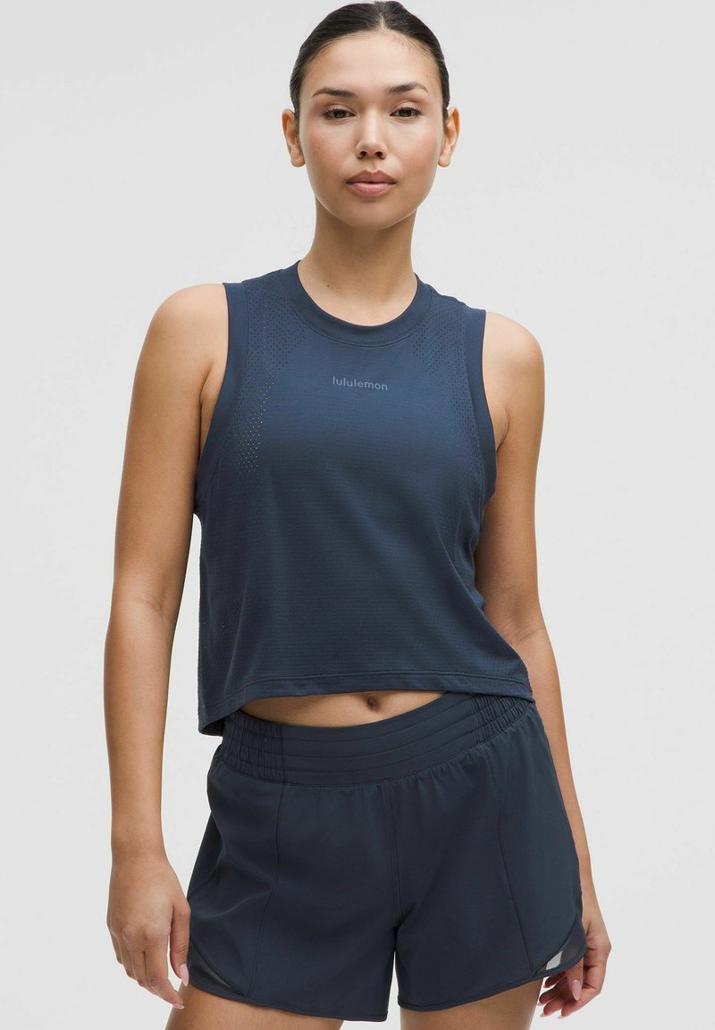 Temno modra športna majica brez rokavov s krojenjem do pasu, okroglo ovratnice in mrežnimi detajli. V kombinaciji z ustreznimi temno modrimi kratkimi hlačami z elastičnim pasom.