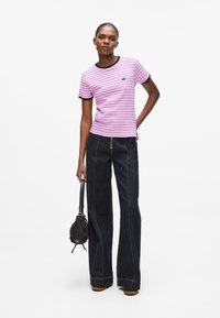 Rosa und weiße gestreifte T-Shirt mit schwarzem Saum, kombiniert mit hoch taillierten, dunkelblauen, weiten Jeans. Das Model hält eine kleine schwarze Tasche.