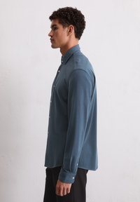 Langslavige knopsluiting blouse van zacht teal stof, met een kraag en beige knopen, met een rechte snit en omgeslagen mouwen.