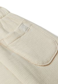 Przyjemny w dotyku, kremowy materiał z teksturą, z kieszonką naszywaną i subtelnym przeszyciem. Na kieszeni znajduje się małe logo jako element wykończenia.