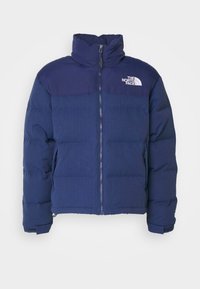 Doudoune bleu marine avec col montant, fermeture éclair frontale, poches latérales, et logo blanc "The North Face" sur la poitrine.