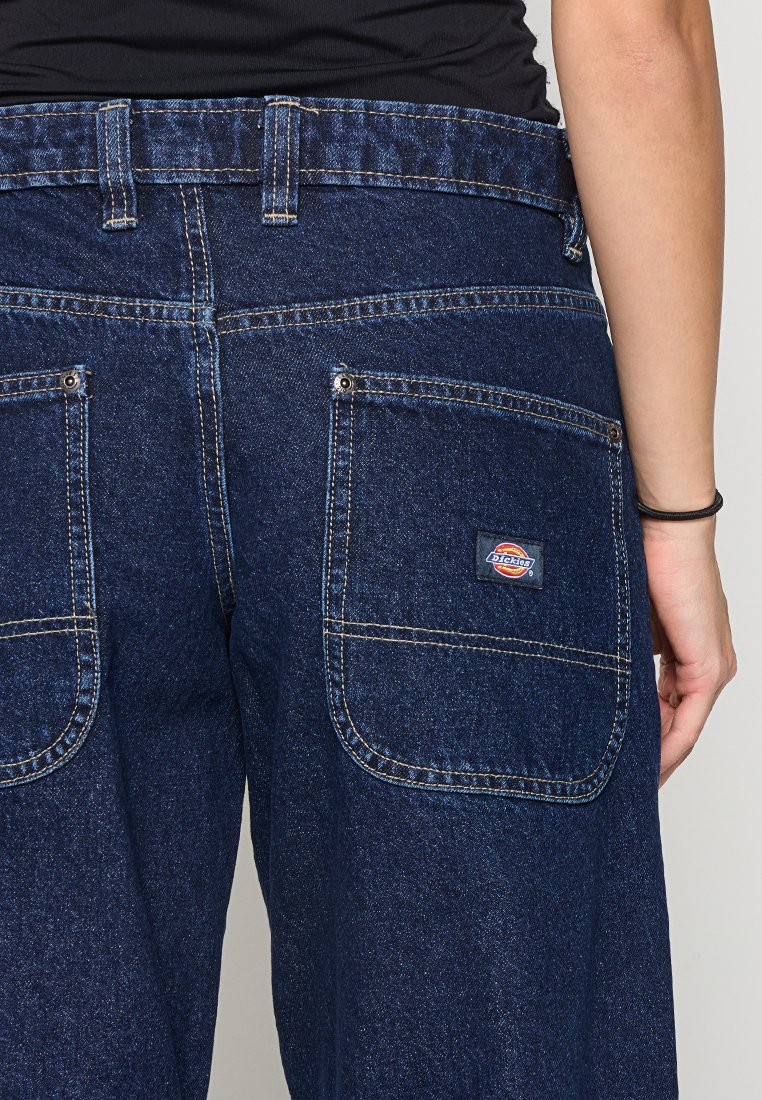 Pantaloni da lavoro in denim blu scuro, con due tasche posteriori, cuciture a contrasto e un'etichetta del marchio sulla tasca destra.