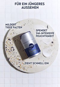 NIVEA Men anti-aging cream in a silver container with a blue label, placed on a circular stone surface, with drops of cream beside it.