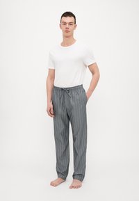 Grijs gestreepte pyjamabroek met een elastische tailleband en trekkoord, gecombineerd met een aansluitend wit T-shirt. Blote voeten, staande pose.