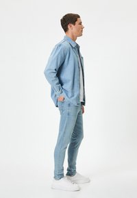 Camisa de mezclilla de color azul claro y jeans a juego, ambos de diseño ajustado. Zapatillas blancas. Textura suave con un aspecto casual.