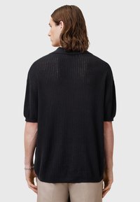 Svart stickad tröja med korta ärmar, med ribbat mönster och en avslappnad passform, sedd bakifrån. Inga synliga mönster eller detaljer.