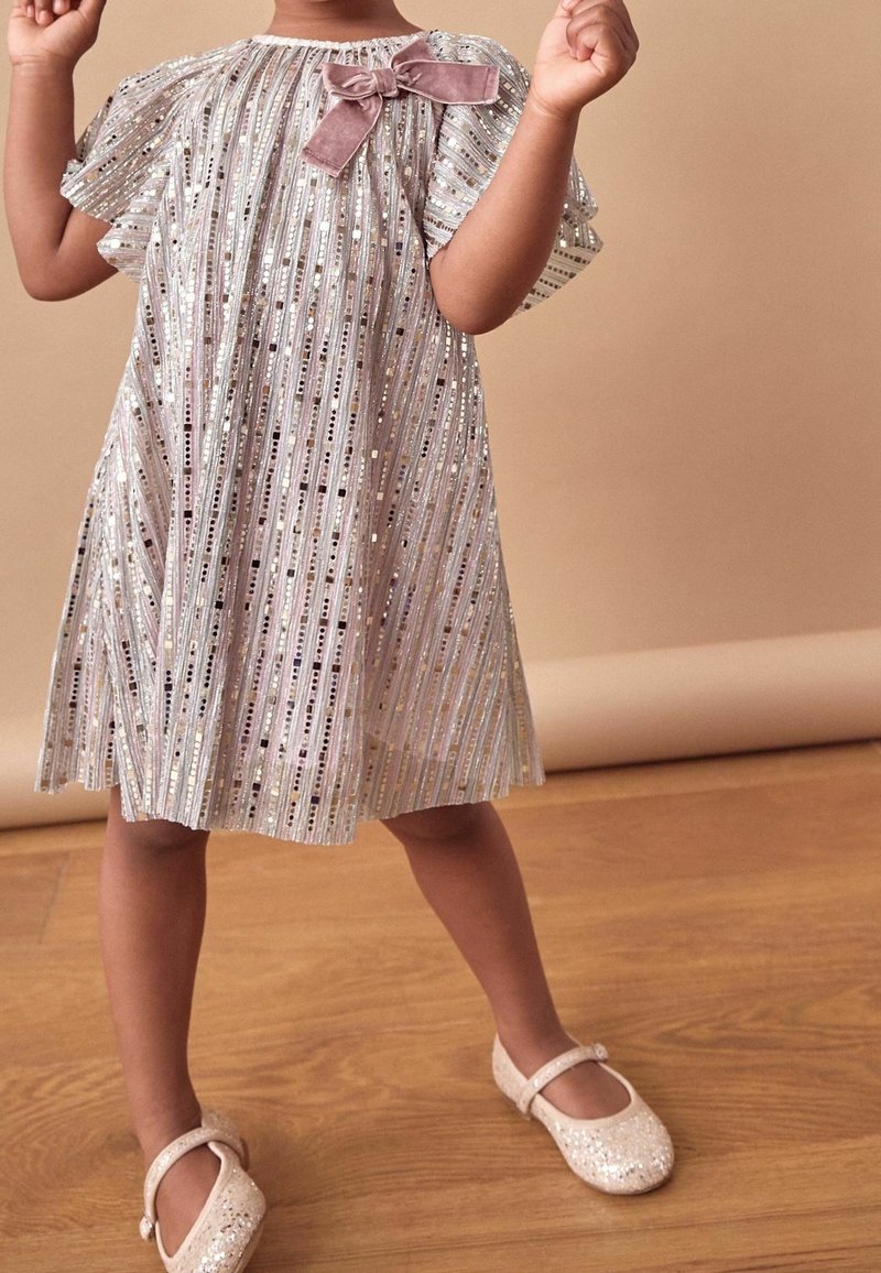 Glittrande silverklänning med horisontella ränder och en rosa sammetssløjfe vid halsen. Glittriga beige ballerinas. Slätt tyg.