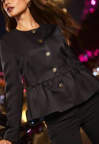 Černá peplum bunda vyrobená ze saténu s kulatým výstřihem, se čtyřmi kovovými knoflíky a dlouhými rukávy. Hladká textilie, přiléhavý střih.