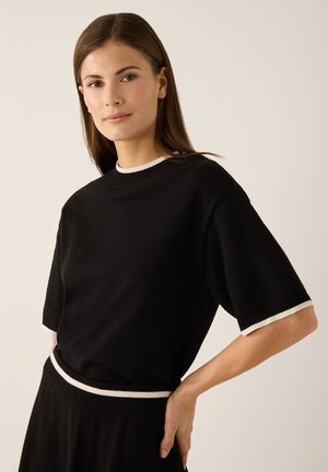 Zwart T-shirt met korte mouwen en een ronde halslijn, afgewerkt met contrasterende witte geribbelde biezen bij de kraag en mouwen. Gladde textuur, losse pasvorm.