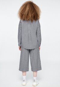 Musta-valkoinen gingham-ruutukuosinen asu, johon kuuluu löysä pitkähiha paita ja lyhyt housut, yhdistettynä valkoisiin lenkkareihin ja nilkkapituisiiin sukkiin.