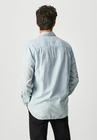 Camicia jeans azzurro chiaro a maniche lunghe con colletto a punta, orlo dritto e polsini con bottoni, che presenta una texture morbida e leggermente sbiadita.