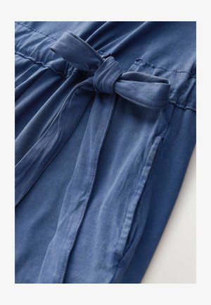 Robe en denim de couleur bleu clair, avec une ceinture nouée, des coutures horizontales et deux poches latérales. Texture lisse, coupe décontractée.