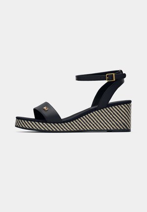 Sandalette noire à talon compensé avec une large sangle, semelle texturée tissée en motif diagonal et une bride de cheville avec une accent de boucle dorée.