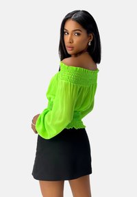 Off-the-shoulder limoen groene blouse met een smocked lijfje en lange, pofy mouwen, gecombineerd met een zwarte minirok. Glad stoftextuur.