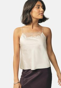 Light beige silk camisole with delicate floral lace trim at the neckline, featuring adjustable straps and a loose, flowing fit.