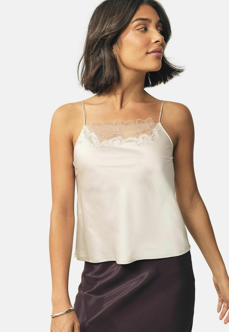 Light beige silk camisole with delicate floral lace trim at the neckline, featuring adjustable straps and a loose, flowing fit.