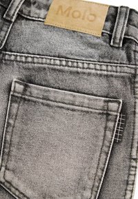 Gros plan d'une poche de jean en denim noir délavé avec des bords cousus et une étiquette de marque en cuir au-dessus de la ceinture indiquant « Molo ».