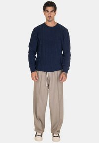 Maglione navy lavorato a maglia con motivo a trecce, abbinato a pantaloni larghi grigi chiari e sneaker bianco e nere. Maniche lunghe, scollatura a girocollo.