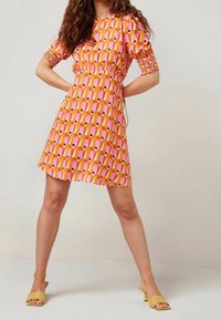 Robe à manches courtes avec un corsage ajusté, une taille élastiquée et un motif géométrique vibrant en rose, orange et noir. Tissu lisse.