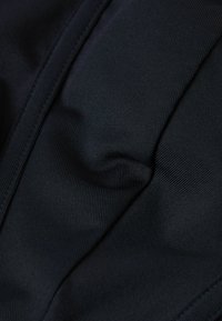 Czarna tkanina z teksturowanym prążkowanym wzorem, z delikatnymi fałdami i suwakiem wzdłuż jednego brzegu, co nadaje jej gładki i elastyczny wygląd.