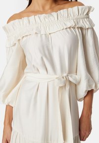 Hvid off-the-shoulder kjole med flæsekrave, ballonærmer, en bundet taljebælte og blødt, struktureret stof.