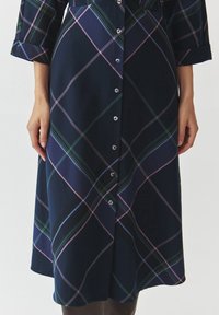 Robe à carreaux navy bleu avec des lignes vertes, roses et bleues. Front à boutons et manches trois-quarts. Tissu doux avec une légère brillance.