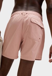 Bañador rosa con cintura elástica, un bolsillo trasero y tela texturizada. Corte corto con bordes rematados.