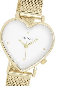 Montre en forme de cœur doré avec un cadran blanc, aiguilles dorées des heures et des minutes, bracelet en maille et nom de marque "OOZOO" imprimé sur le cadran.