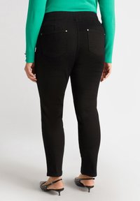 Jeans negros ajustados con dos bolsillos traseros y detalles de metal plateado. Combinados con un suéter verde y tacones negros con tachuelas.