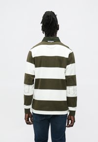 Koszula w paski z długim rękawem w ciemnozielono-białej kolorystyce. Posiada kołnierzyk, łatki na łokciach oraz metkę z tyłu. Wykonana z teksturowanej bawełny.