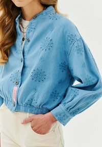 Zkrácená modrá džínsová bunda s vyšitými květinovými vzory, stříbrnými knoflíky a elastickým pasem. Lehká textura s dlouhými rukávy.