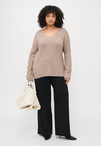 V-neck, long-sleeve sweater in light brown knit, paired with black wide-leg pants, holding a cream tote bag with thin straps.