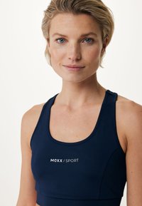 Sostenedor deportivo de color navy, hecho de un tejido elástico con escote en forma de scoop, presentando un logo blanco en la parte frontal y un diseño sin costuras para mayor comodidad.